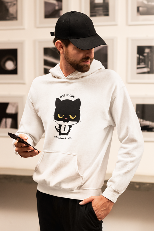 Bearded man holding smartphone in a cozy home setting wearing white hoodie with black cat graphic in tie and one house one boss me slogan